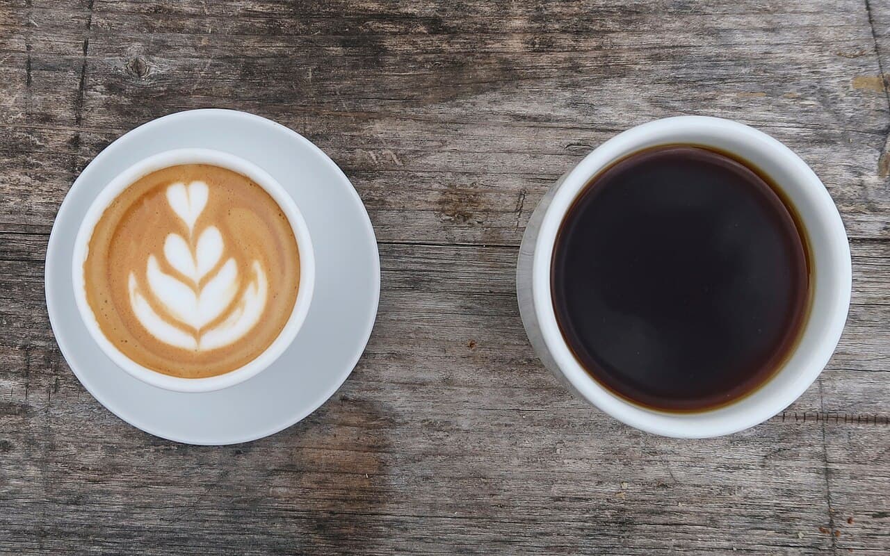 A latte and a black coffee on a wooden table